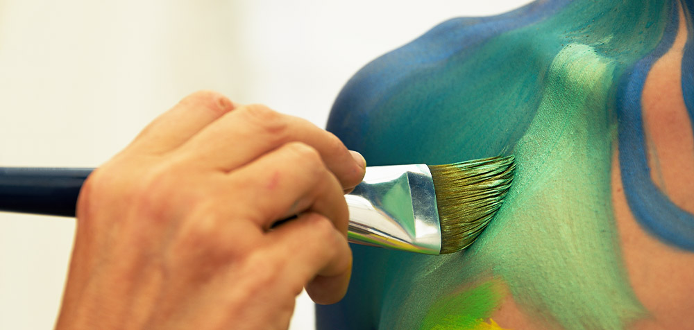 Mano di un artista con pennello che colora la spalla di una modella